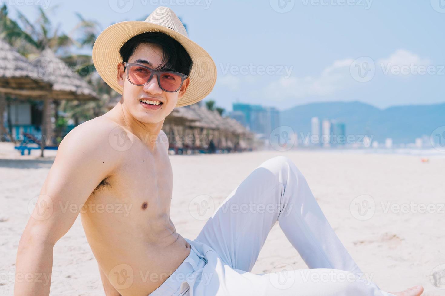 jovem asiático sem sela sentado na areia a olhar para o mar foto