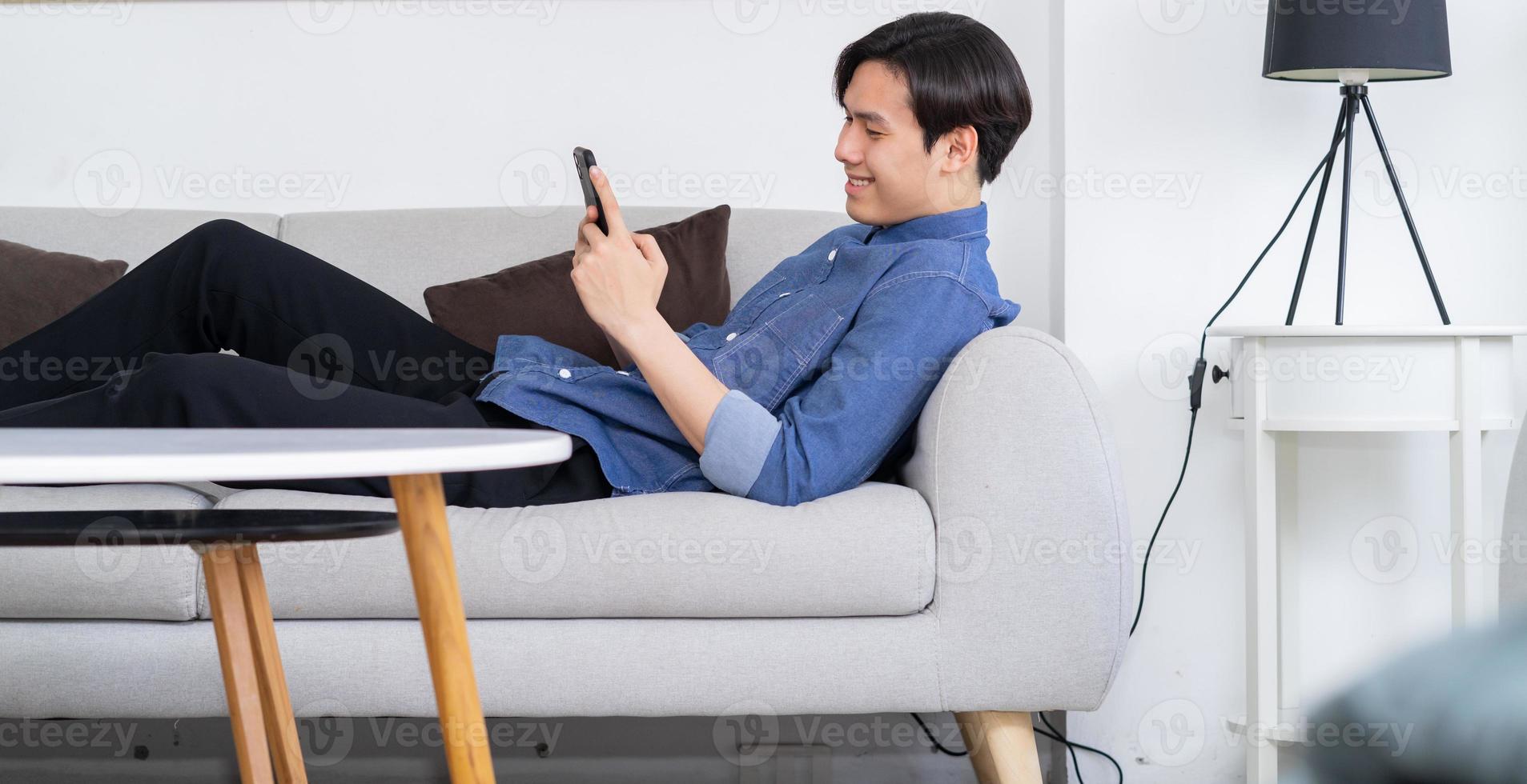 jovem asiático deitado no sofá e usando o telefone foto