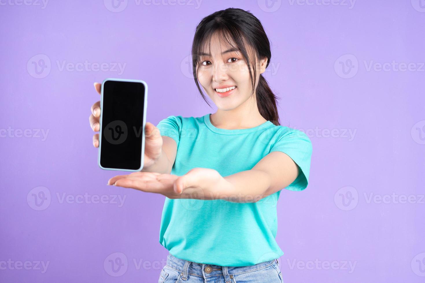 jovem garota asiática com camisa ciano usando o telefone no fundo roxo foto