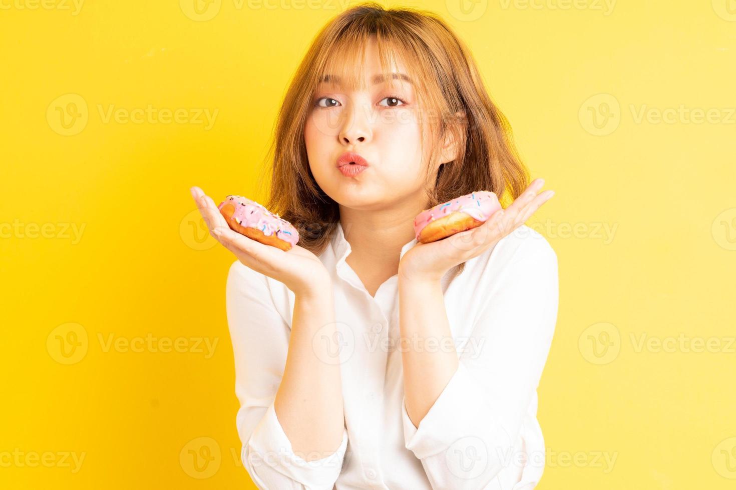 jovem asiática segurando uma rosquinha com uma expressão alegre no fundo foto