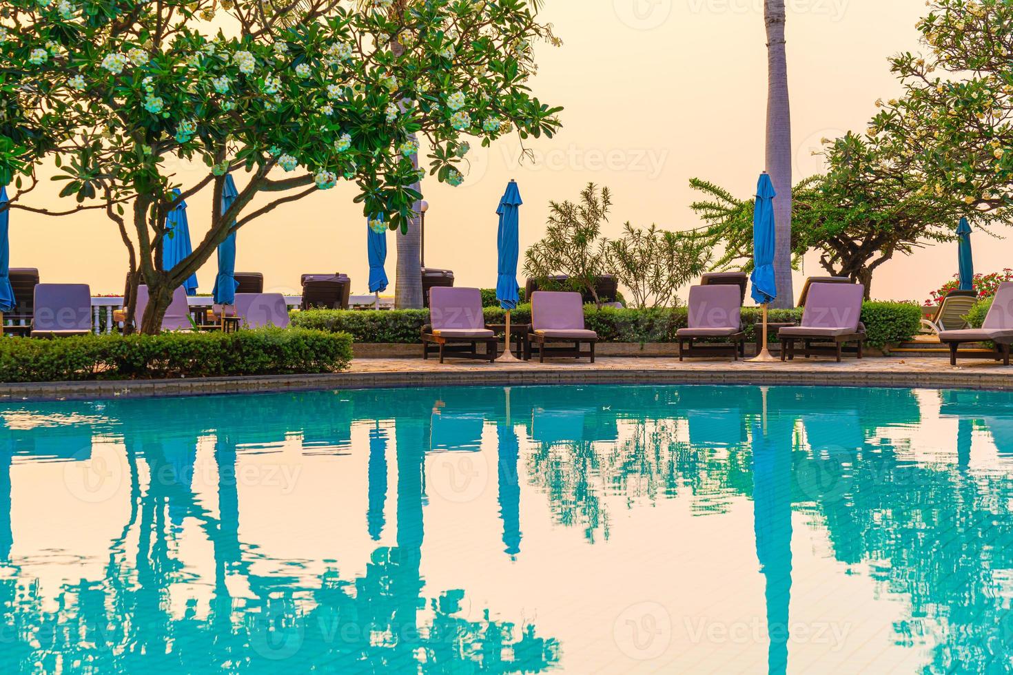 cadeiras de praia ou camas de piscina com guarda-sóis ao redor da piscina na hora do pôr do sol foto