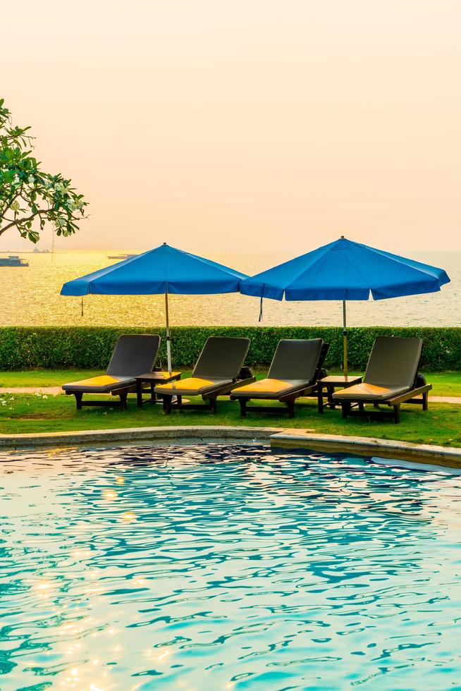 cadeiras de praia ou camas de piscina com guarda-sóis ao redor da piscina na hora do pôr do sol foto