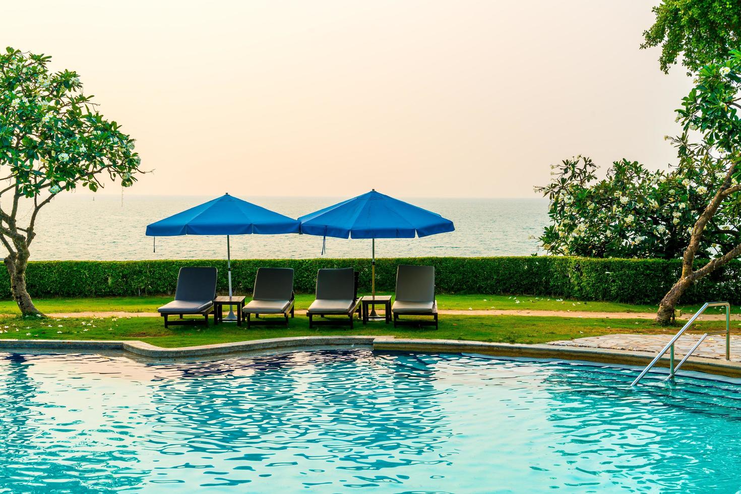 cadeiras de praia ou camas de piscina com guarda-sóis ao redor da piscina na hora do pôr do sol foto