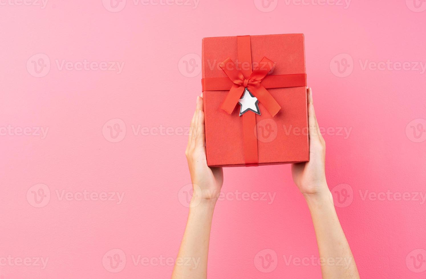 mãos segurando uma caixa de presente vermelha em fundo rosa foto