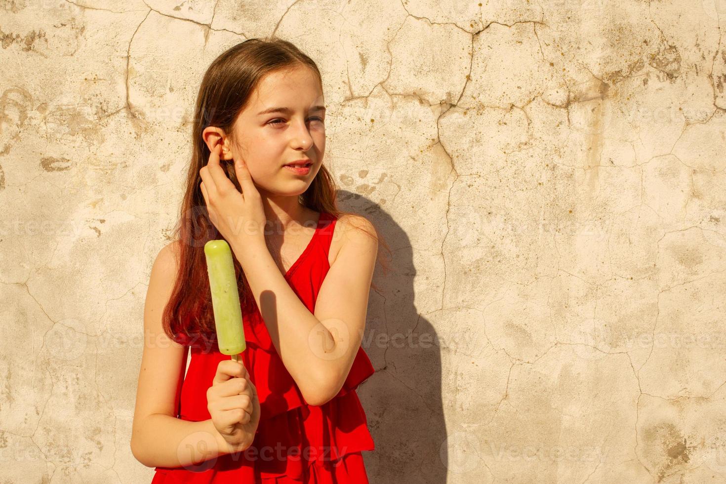 uma menina de 10 ou 11 anos em um dia quente e abafado em um vestido vermelho. adolescente de verão com sorvete. foto