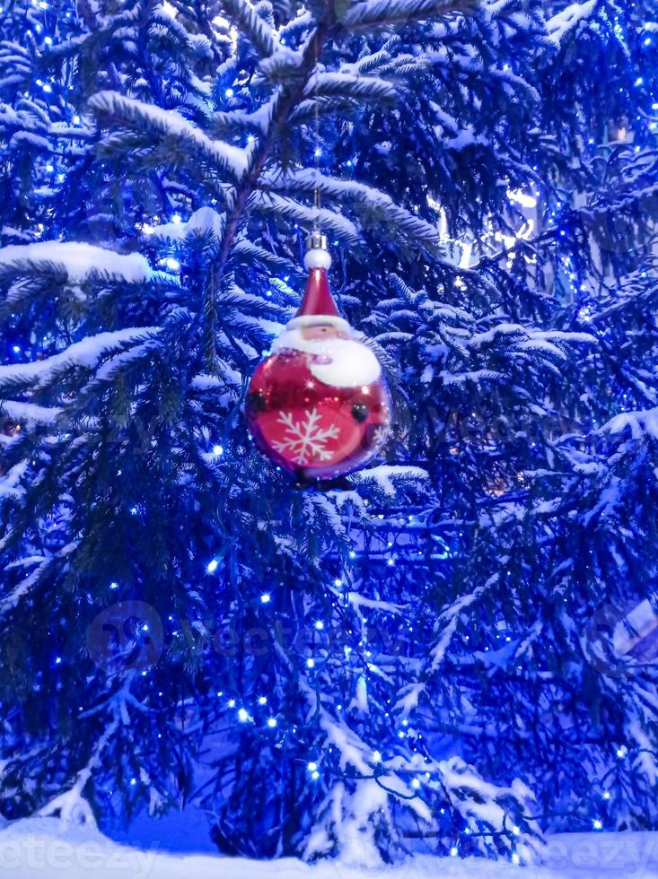 abeto vermelho nevado com uma guirlanda de luzes e uma bola vermelha em forma de papai noel foto