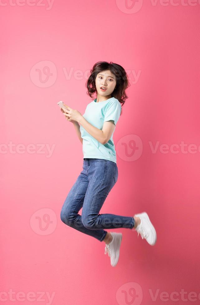 jovem asiática segurando o telefone pulando com uma expressão alegre foto