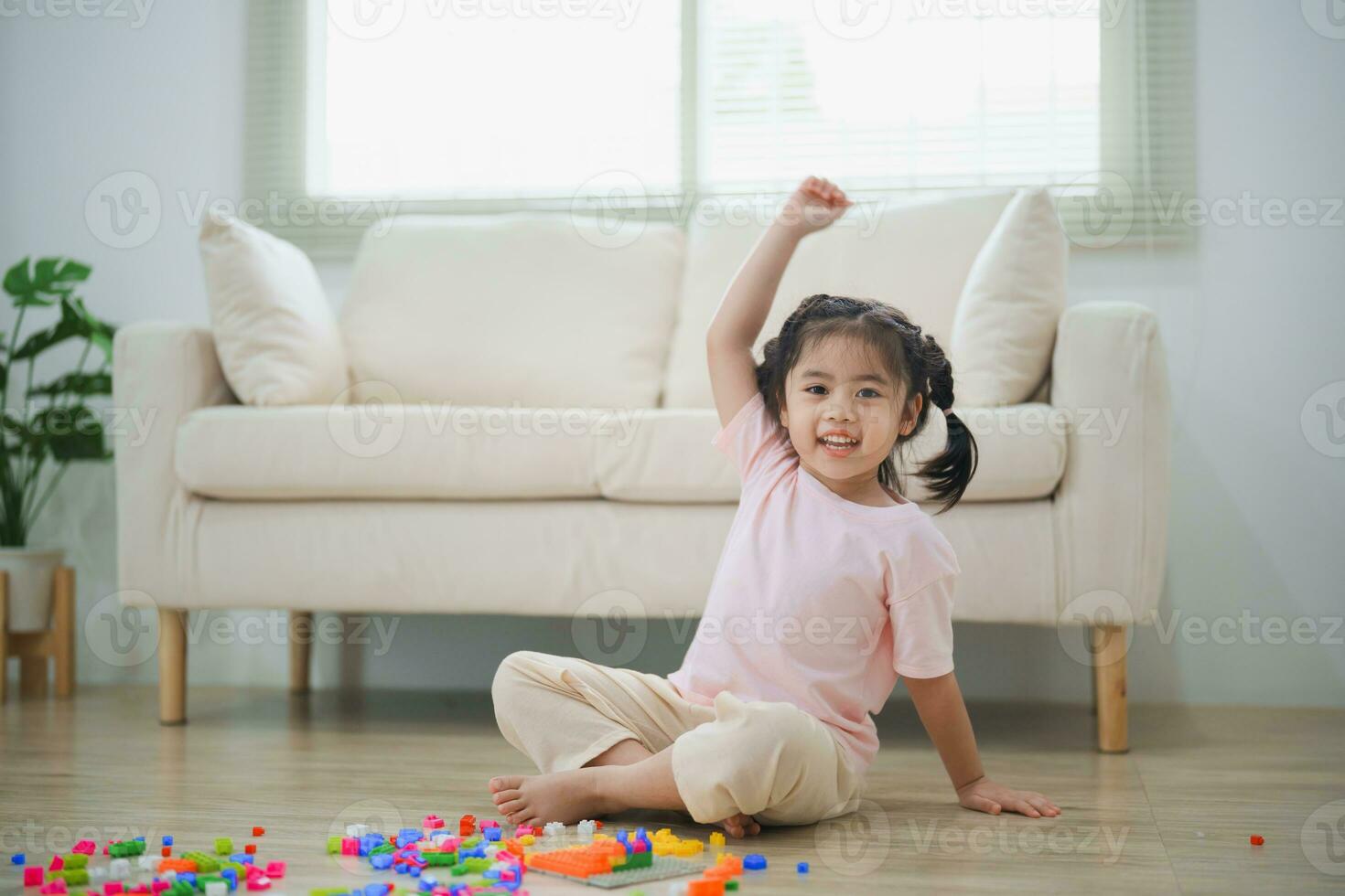 alegre ásia menina feliz e sorridente levantar dela mão jogando colorida Lego brinquedos, sentado em a vivo quarto chão, criativamente jogando com Lego, construção colorida estruturas criatividade Imagine. foto