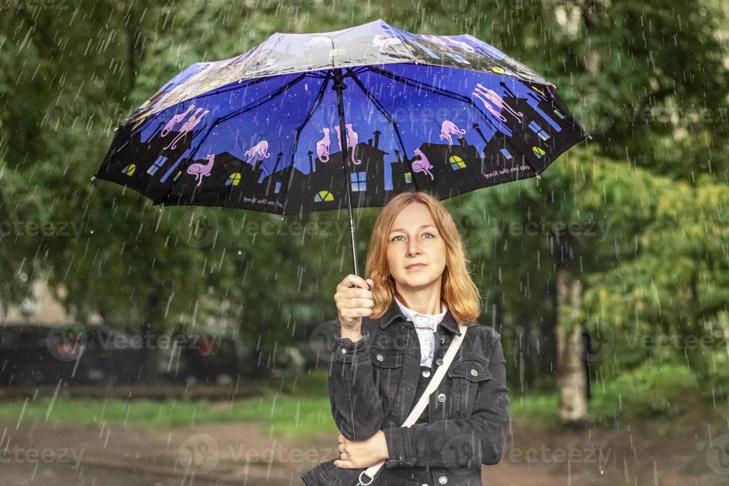 uma jovem fica na chuva na rua sob um guarda-chuva. dia chuvoso foto