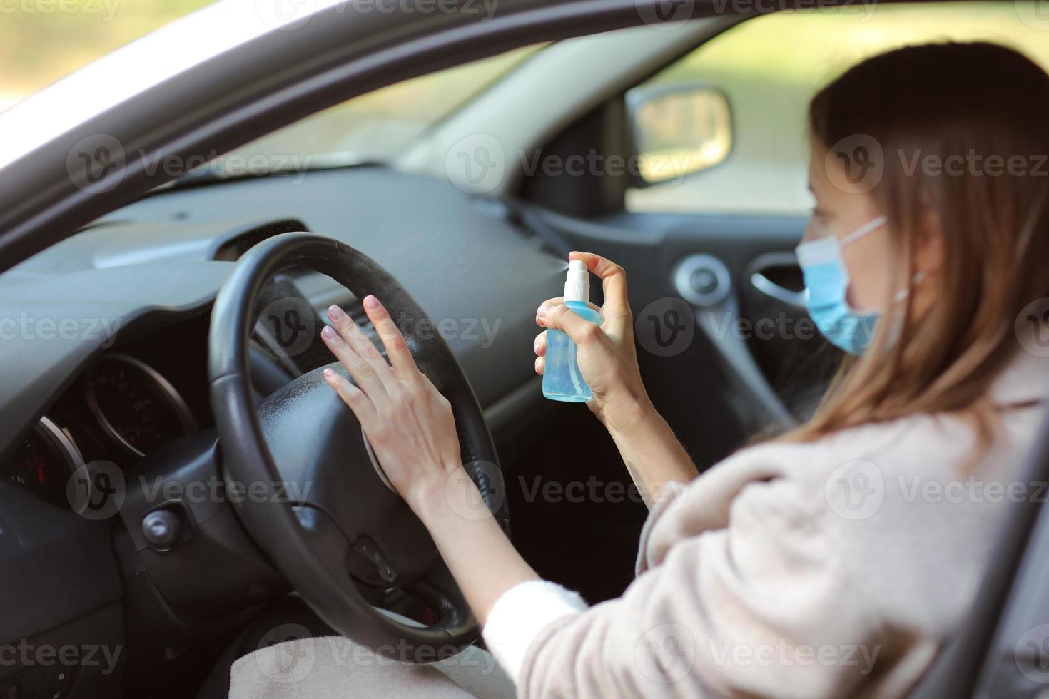 pulverizando spray desinfetante antibacteriano disponível no carro, conceito de controle de infecção. desinfetante para prevenir o coronavírus, covid-19, gripe. garrafa de spray. mulher usando máscara protetora médica, dirigindo um carro. foto