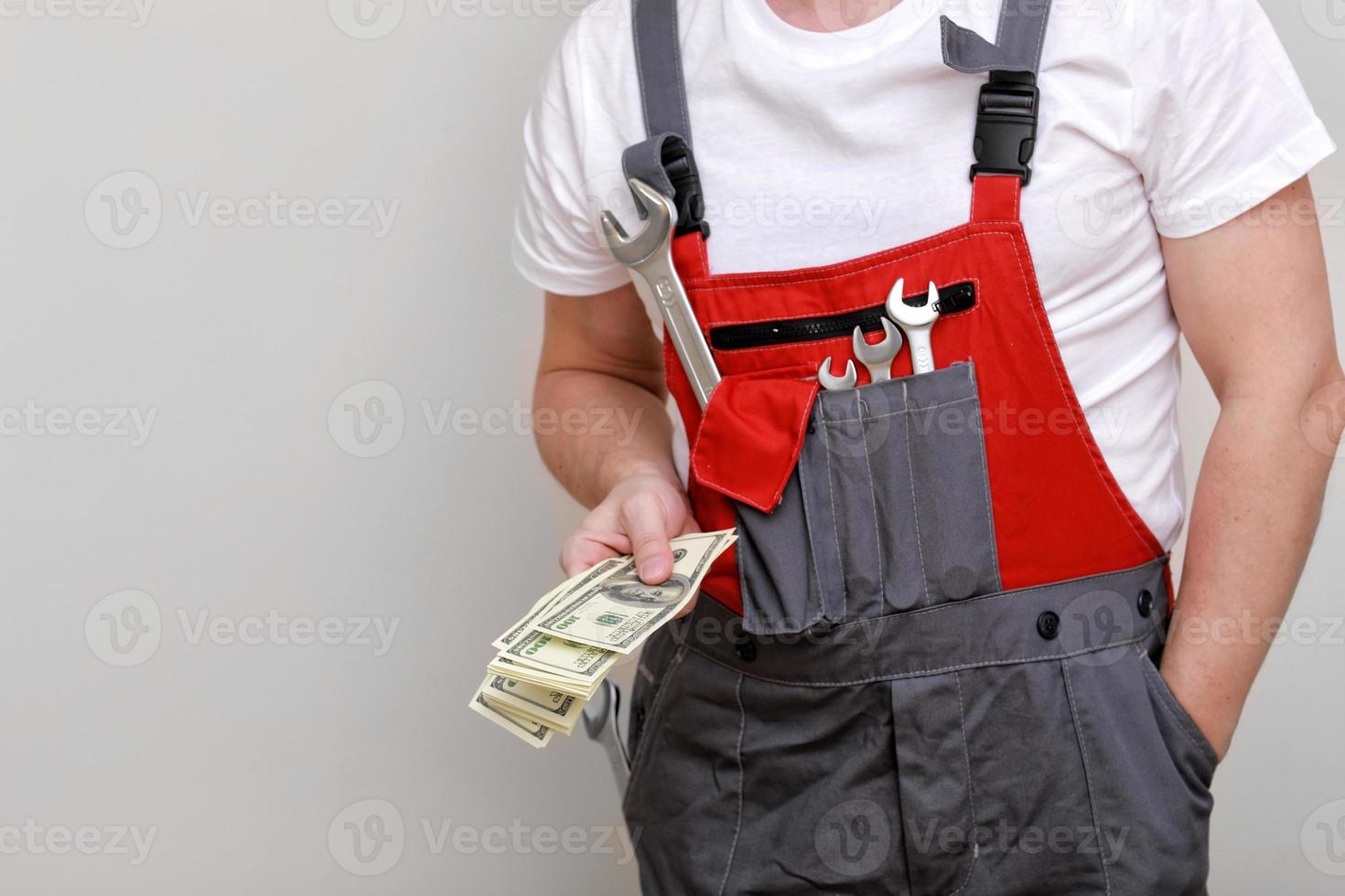 foto recortada de trabalhador em uniforme vermelho, capacete de proteção segurando o pacote de dólares, dinheiro em espécie em fundo branco. trabalhador masculino para propaganda. crise econômica mundial e o conceito de perda de emprego.