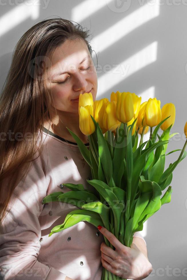 mulher com tulipas. jovem fêmea com estilo de vida de retrato natural de tulipa de flores amarelas perto de fundo branco. foto