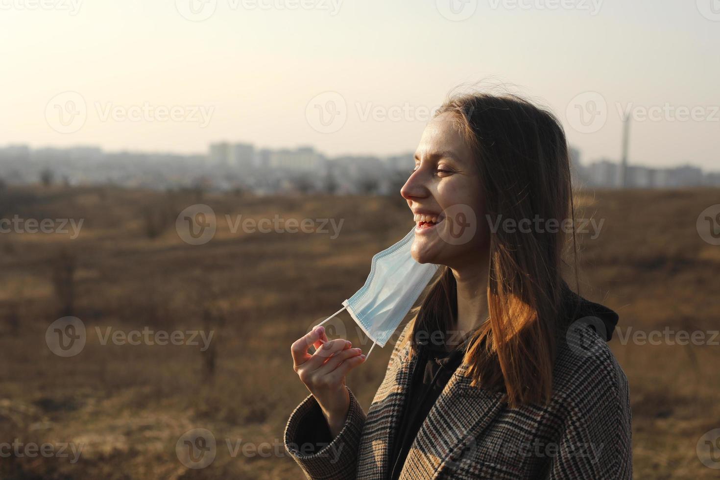 jovem sorridente remove a máscara médica do rosto. término da quarentena, coronavírus. mulher protegendo do coronavírus. covid19. tempo feliz, ar fresco foto