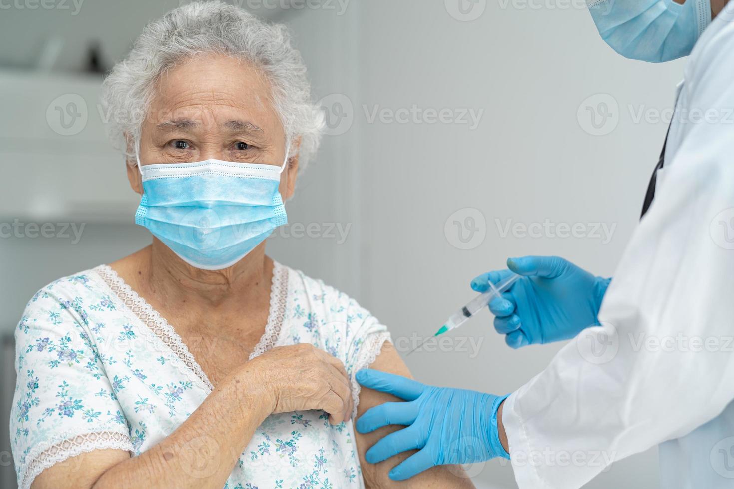 mulher idosa asiática sênior usando máscara facial recebendo vacina de covid-19 ou coronavírus pelo médico fazer injeção. foto