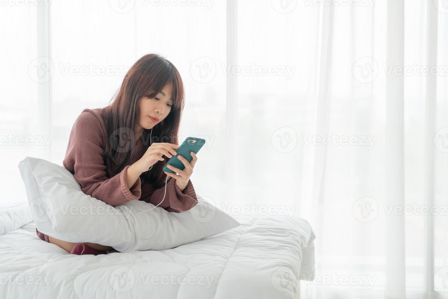 mulher asiática jogando smartphone na cama foto