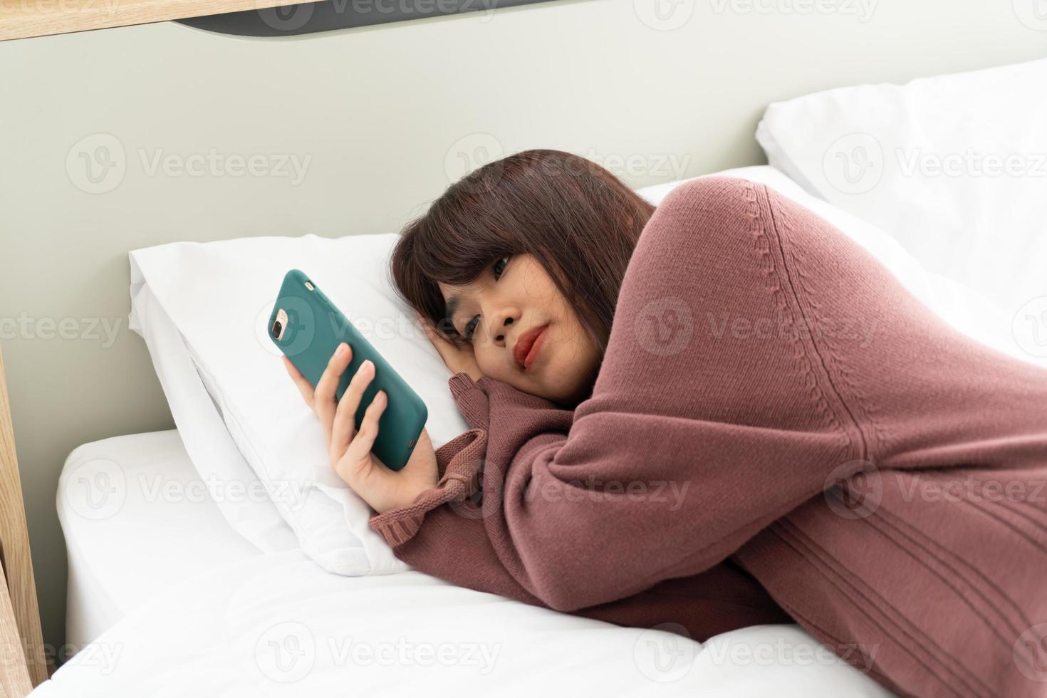 mulher asiática jogando smartphone na cama foto