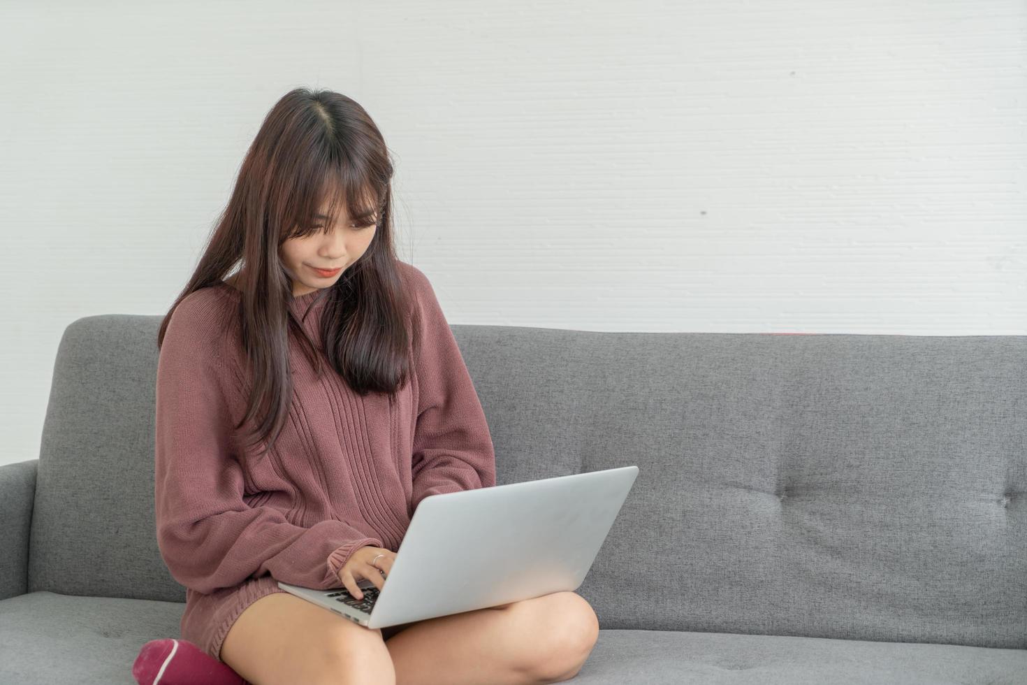 linda mulher asiática usando laptop no sofá da sala foto