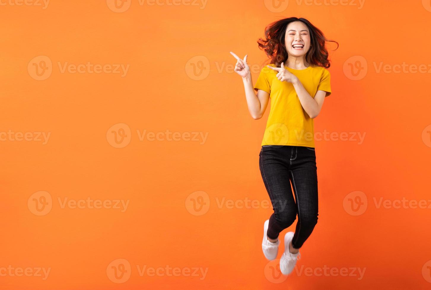 jovem mulher asiática pulando em um fundo laranja foto