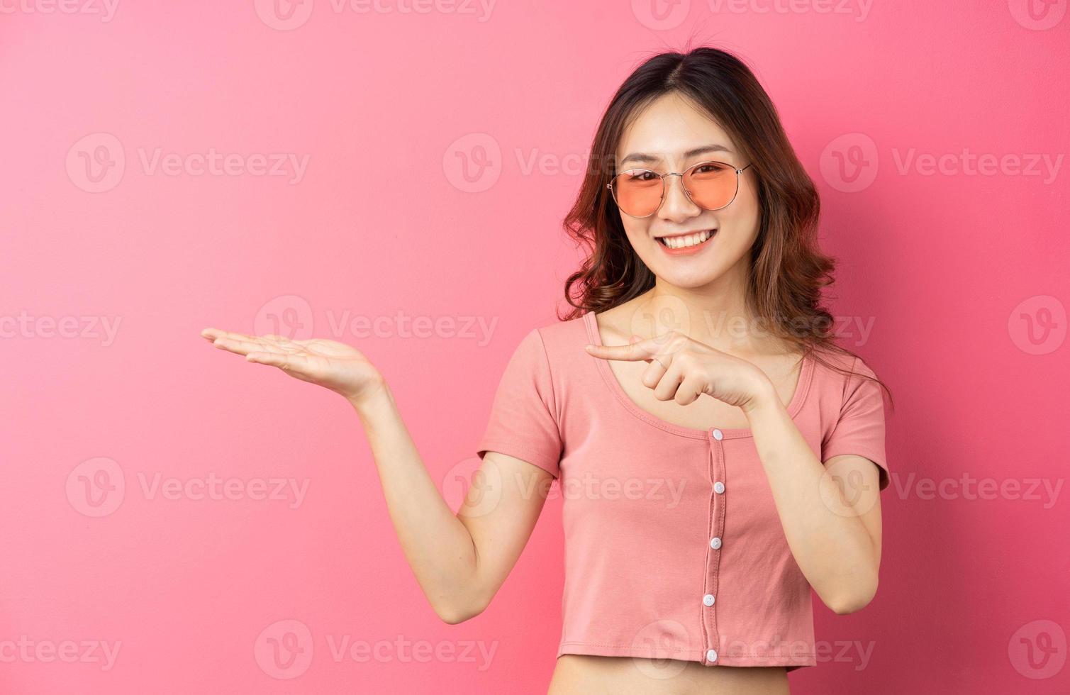 jovem mulher asiática usando óculos com uma expressão alegre em um fundo rosa foto