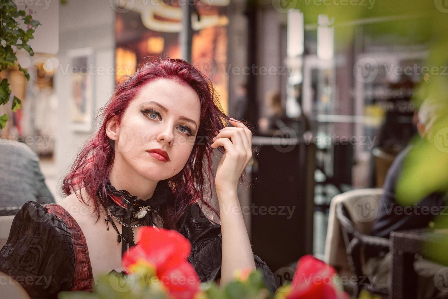 jovem mulher ruiva linda sentada em um café ao ar livre, vestida com roupas da moda retrô. foto