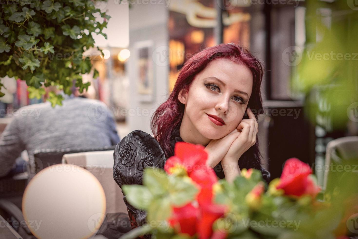 jovem mulher ruiva linda sentada em um café ao ar livre, vestida com roupas da moda retrô. foto