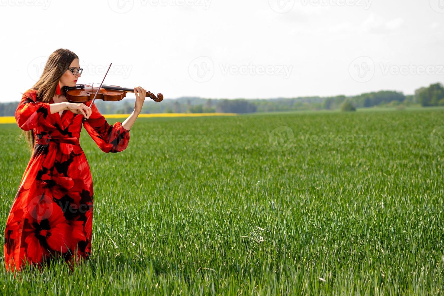 jovem com um vestido vermelho tocando violino em um prado verde - imagem foto