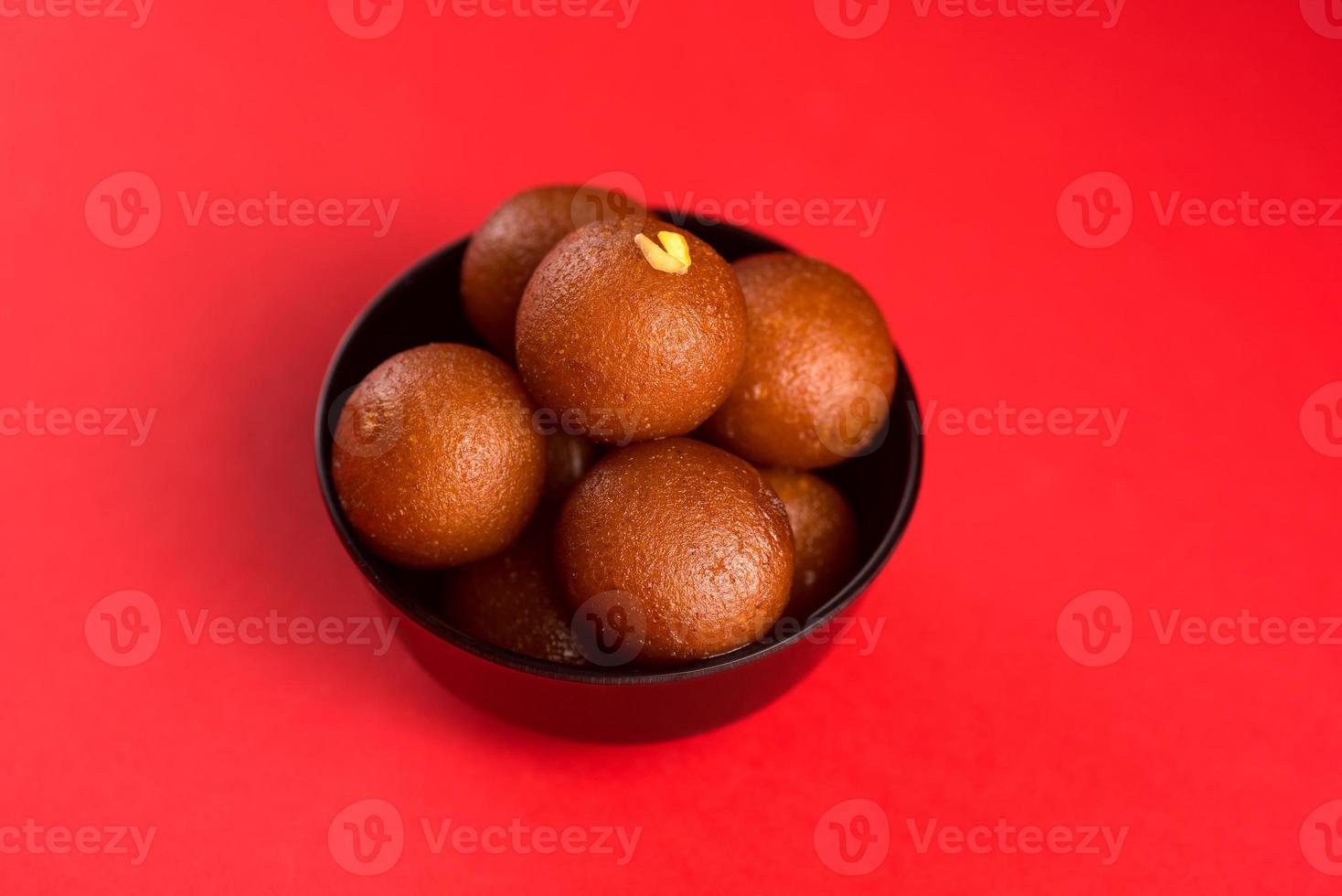 gulab jamun em tigela preta sobre fundo vermelho. sobremesa indiana ou prato doce. foto