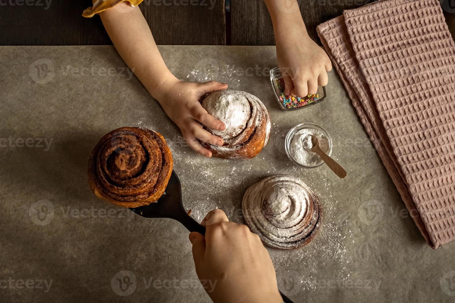 as mãos das crianças na moldura polvilham um pão fresco assado com canela e granulado de massa foto