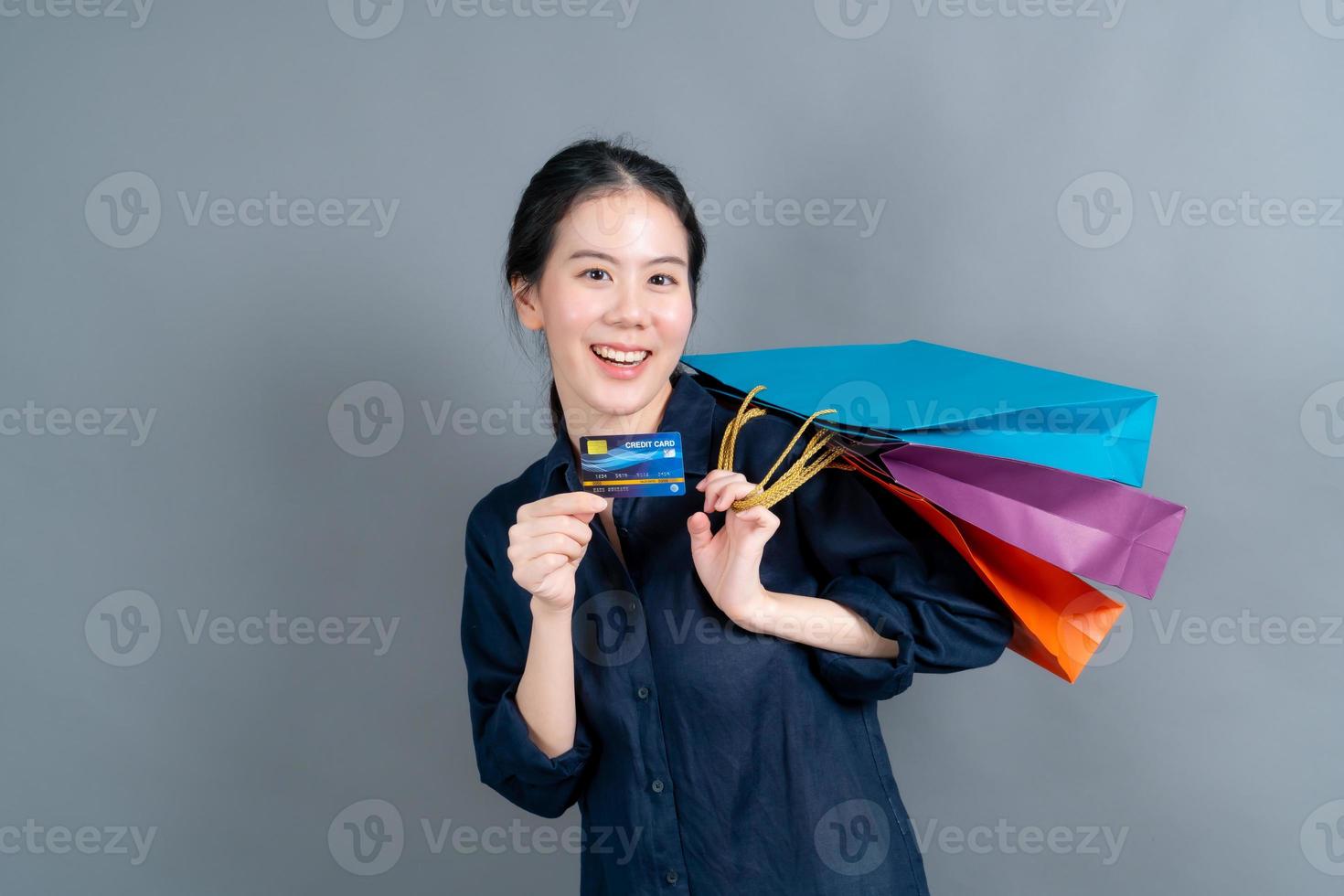 linda mulher asiática com sacolas de compras e apresentando cartão de crédito foto