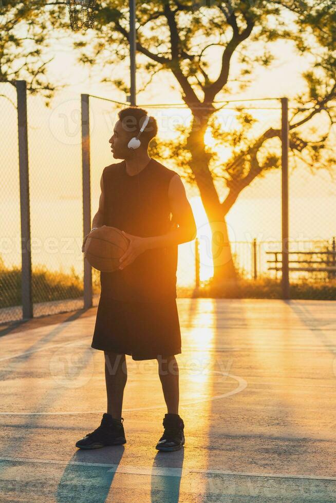 Preto homem fazendo Esportes, jogando basquetebol em nascer do sol, ativo estilo de vida, ensolarado verão manhã foto