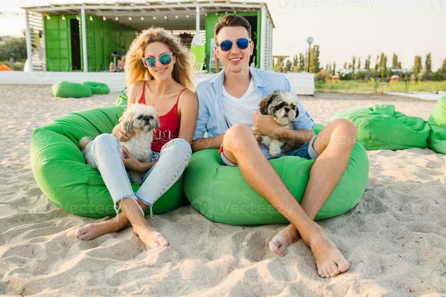 jovem atraente sorridente casal tendo Diversão em de praia jogando com cachorros foto