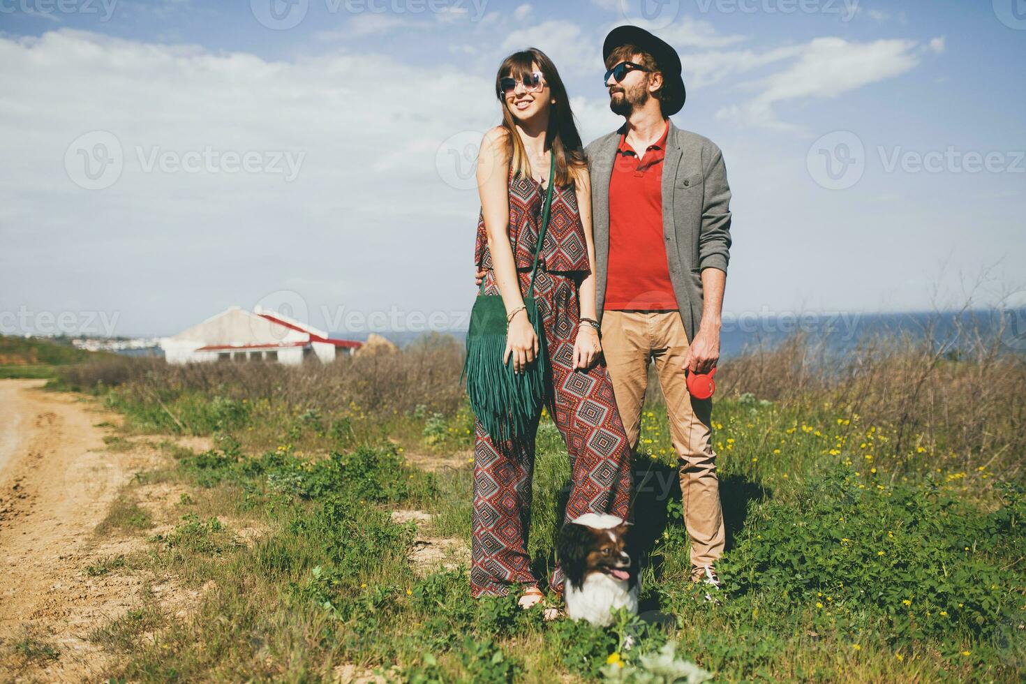 feliz jovem à moda hipster casal dentro amor caminhando com cachorro dentro campo foto