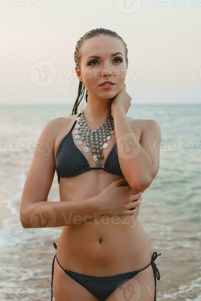 jovem lindo loiro mulher banhos de sol em areia de praia dentro bikini natação terno, vintage colar foto