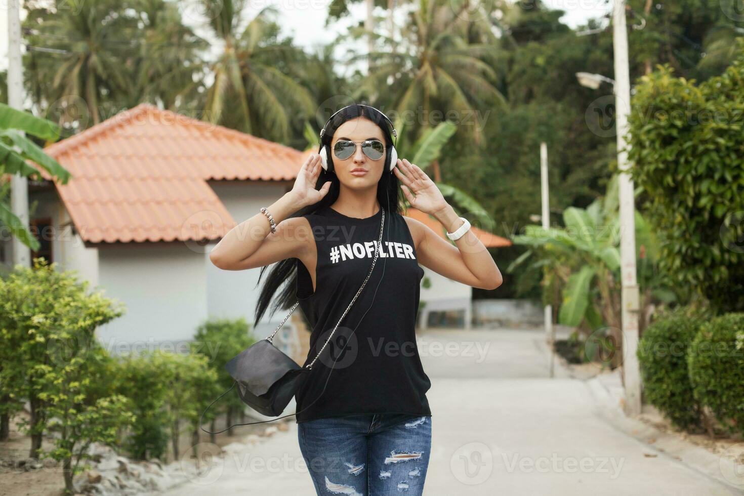 jovem à moda hipster mulher dentro Preto camiseta, jeans, ouvindo para música em fones de ouvido foto