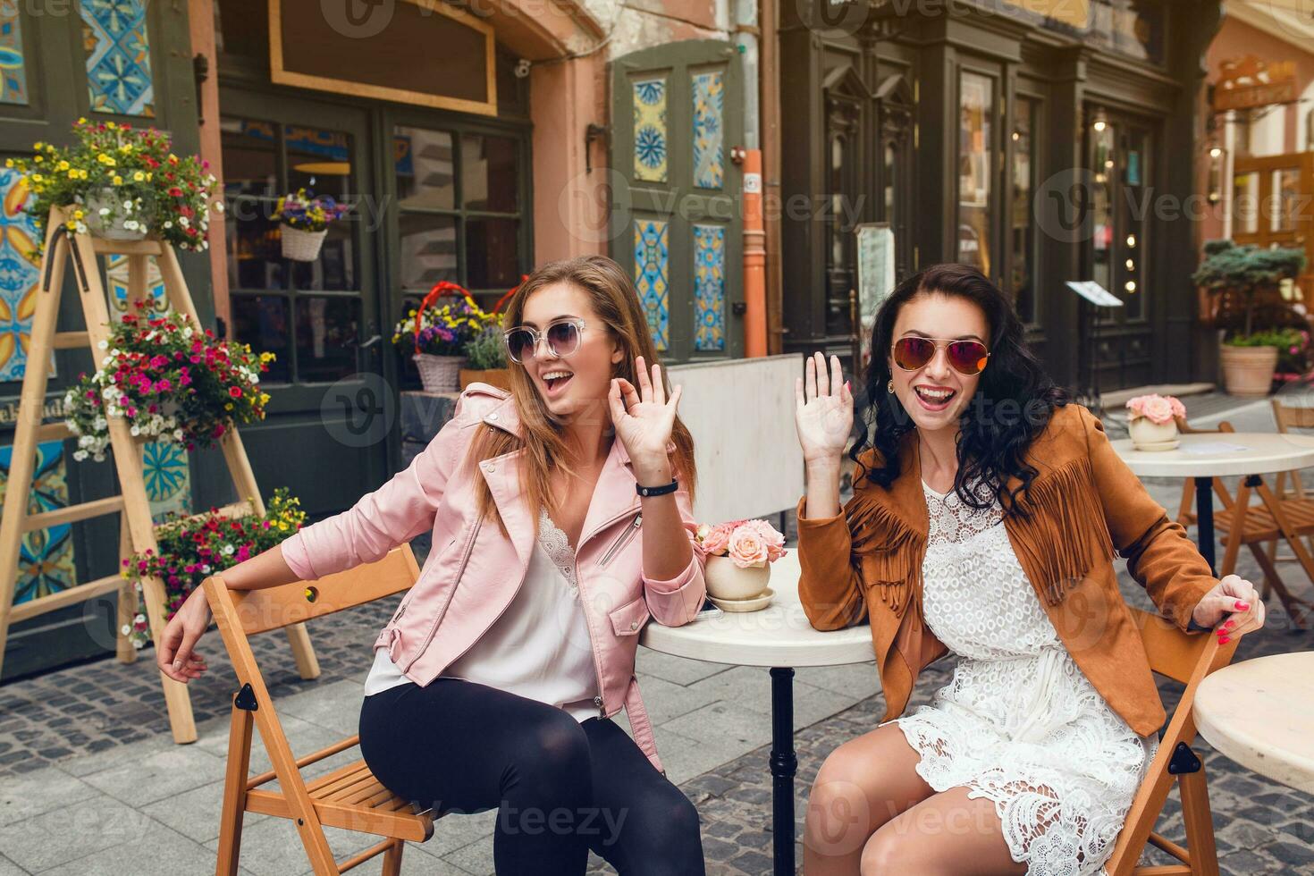 dois jovem à moda mulheres sentado às cafeteria, conversando, bisbilhotice, à moda na moda equipamento foto