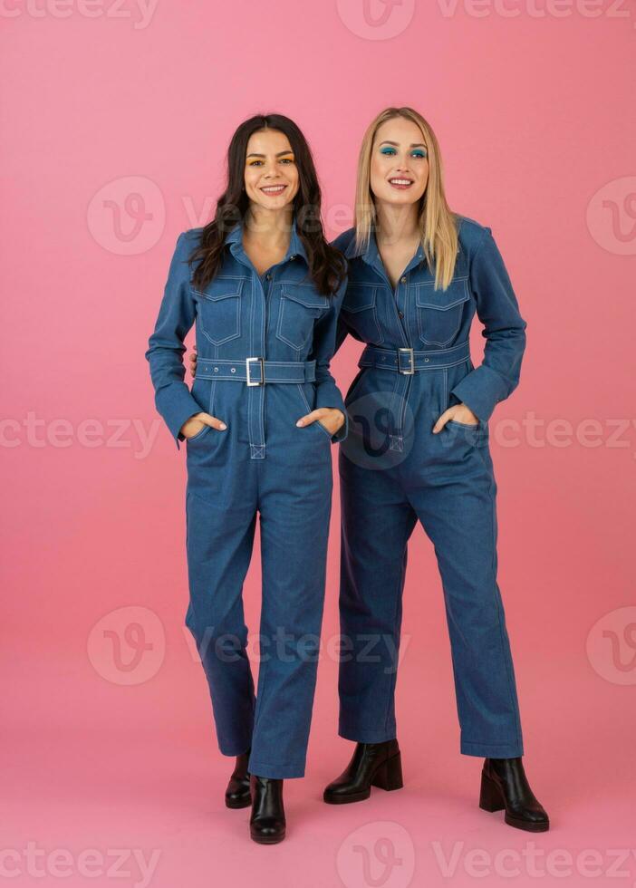 dois animado atraente menina amigos ativo mulheres posando em Rosa fundo dentro jeans No geral tendo Diversão juntos moda tendência foto