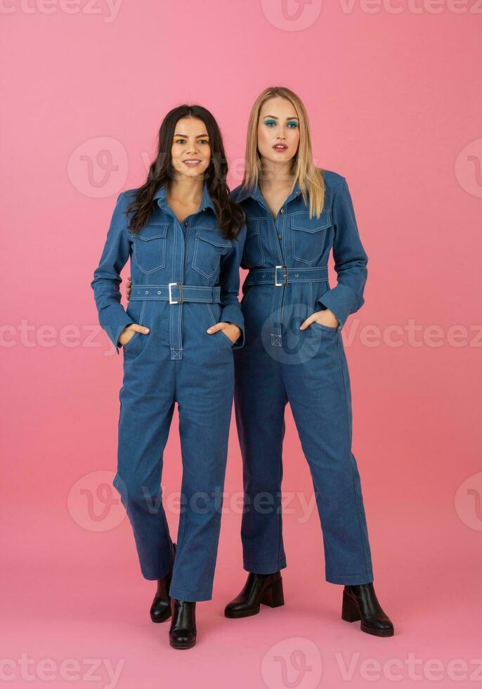 dois animado atraente menina amigos ativo mulheres posando em Rosa fundo dentro jeans No geral tendo Diversão juntos moda tendência foto