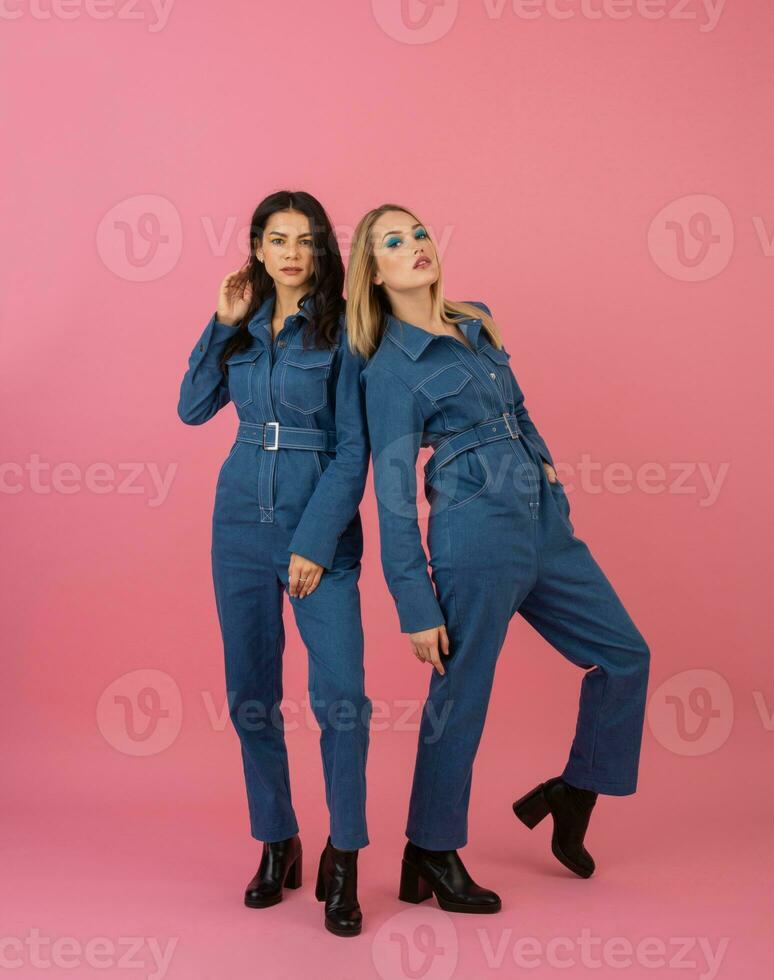 dois animado atraente menina amigos ativo mulheres posando em Rosa fundo dentro jeans No geral tendo Diversão juntos moda tendência foto