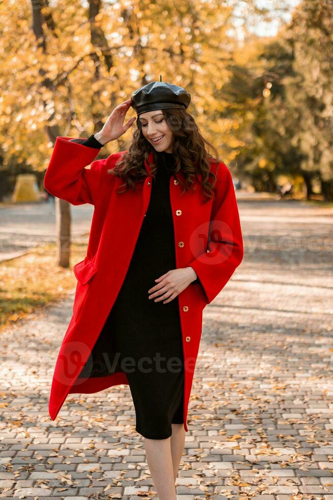 atraente à moda mulher caminhando dentro parque vestido dentro caloroso vermelho casaco foto