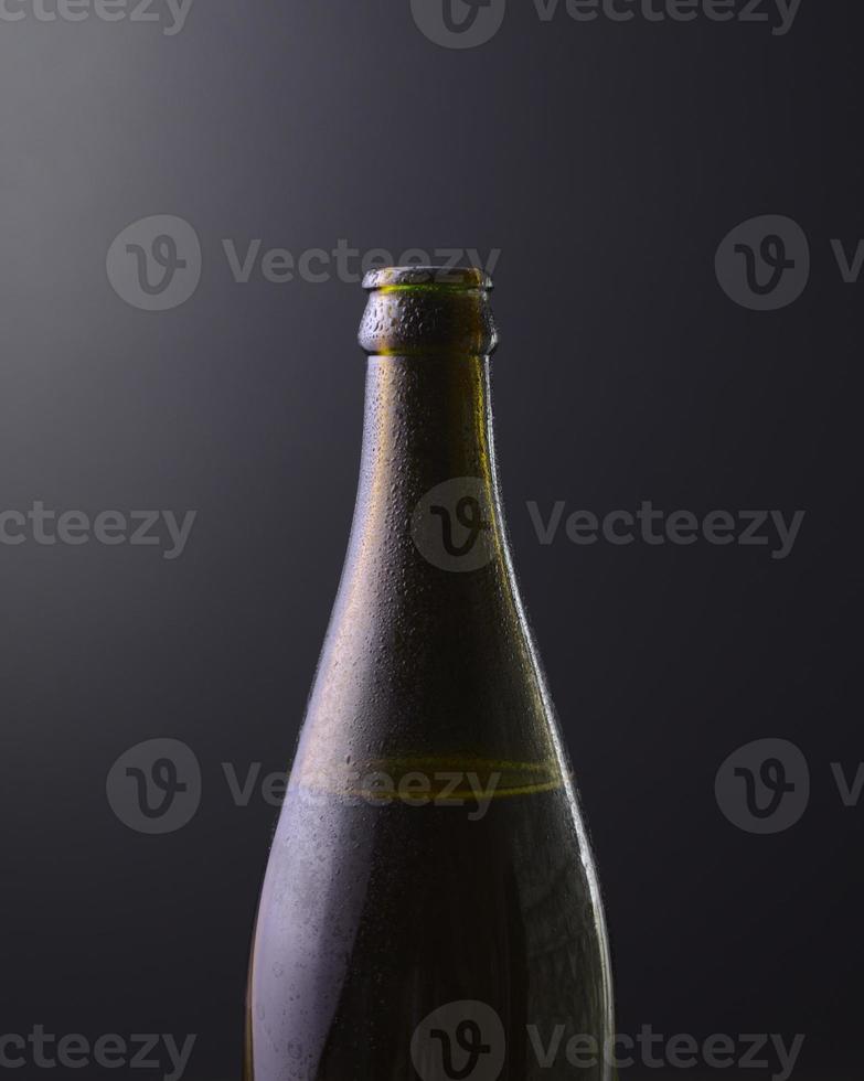 vista frontal de uma garrafa de cerveja gelada com fundo preto escuro com cores gradientes roxas. bebida alcoólica gelada, conceito do dia internacional da cerveja. foto