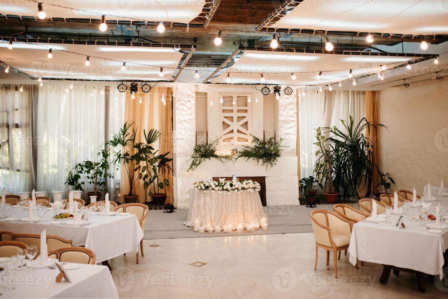 o presidium dos noivos no salão de banquetes do restaurante é decorado com velas e plantas verdes foto