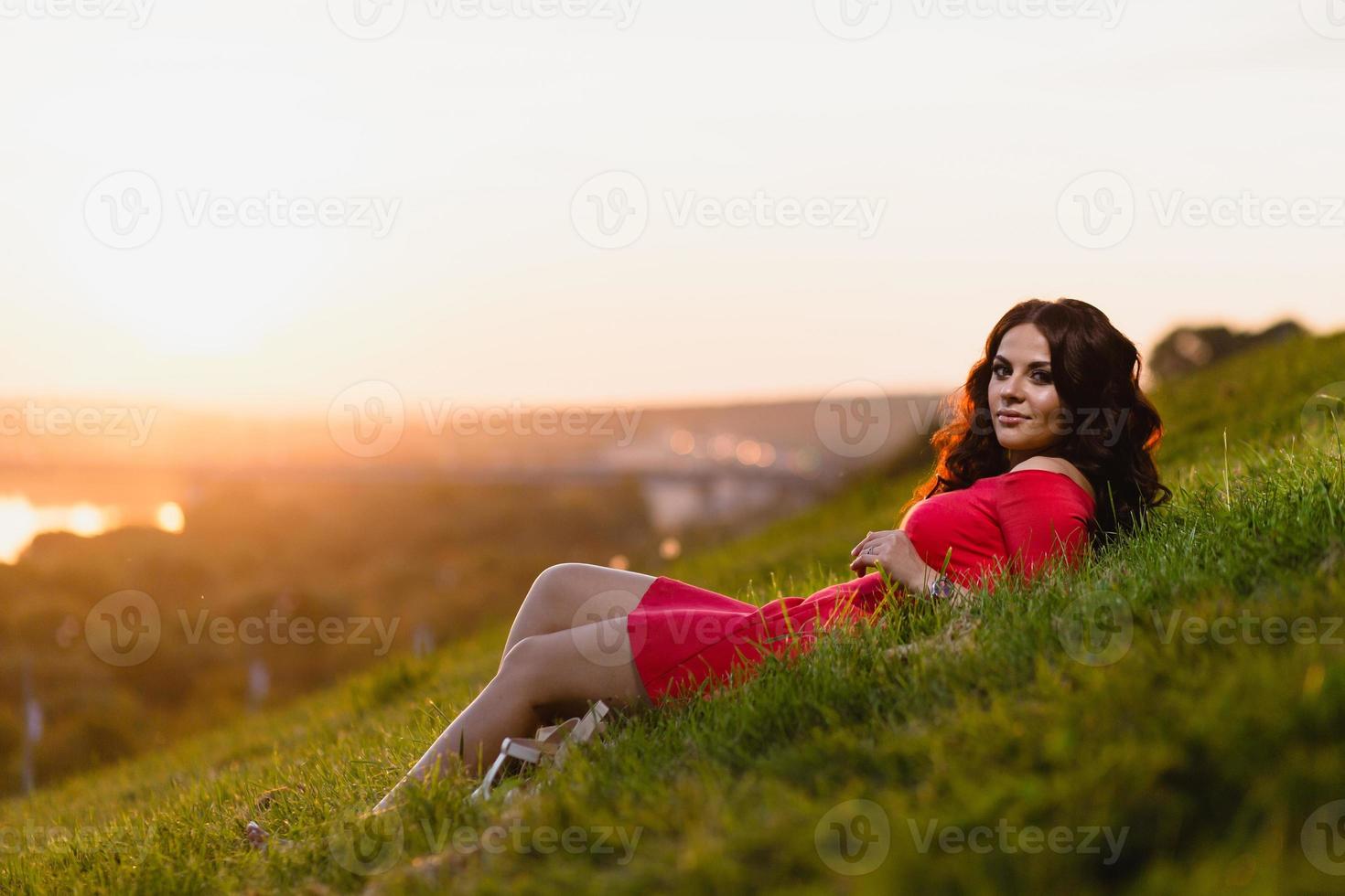 linda jovem sentada em uma encosta coberta com grama verde foto