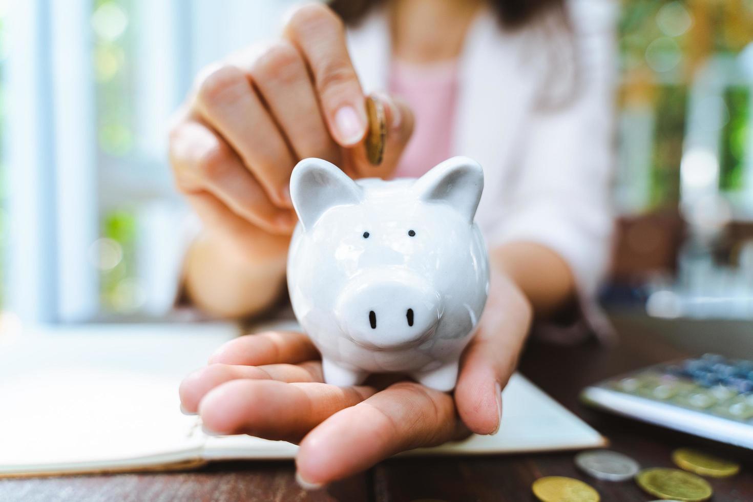 close up da mão de mulher de negócios, colocando moedas de dinheiro no cofrinho para economizar dinheiro. economizando dinheiro e conceito financeiro foto