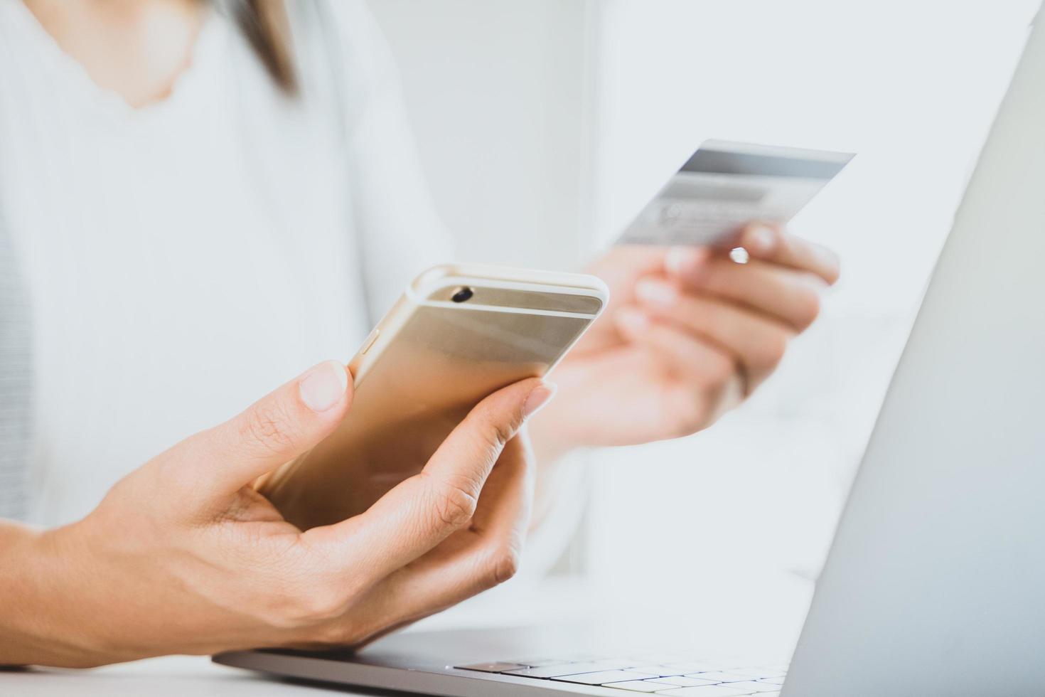 mão de mulher segurando o cartão de crédito e telefone inteligente usando laptop. paymet online, conceito de compras online foto