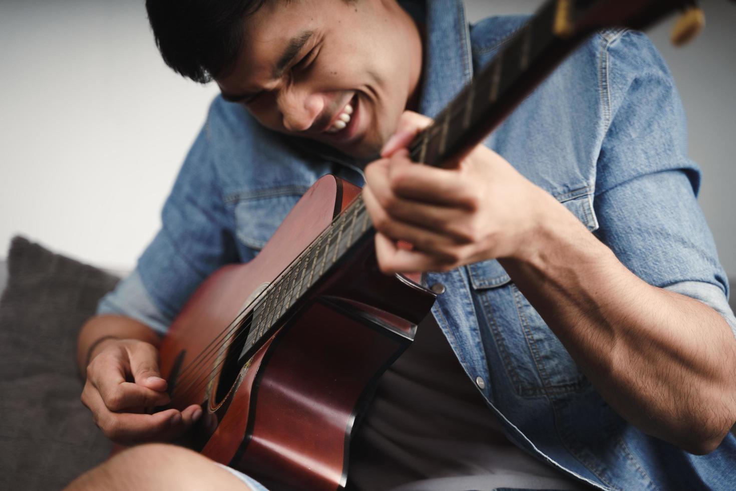 Desfrute de um belo homem asiático praticando ou tocando violão no sofá da sala de estar foto