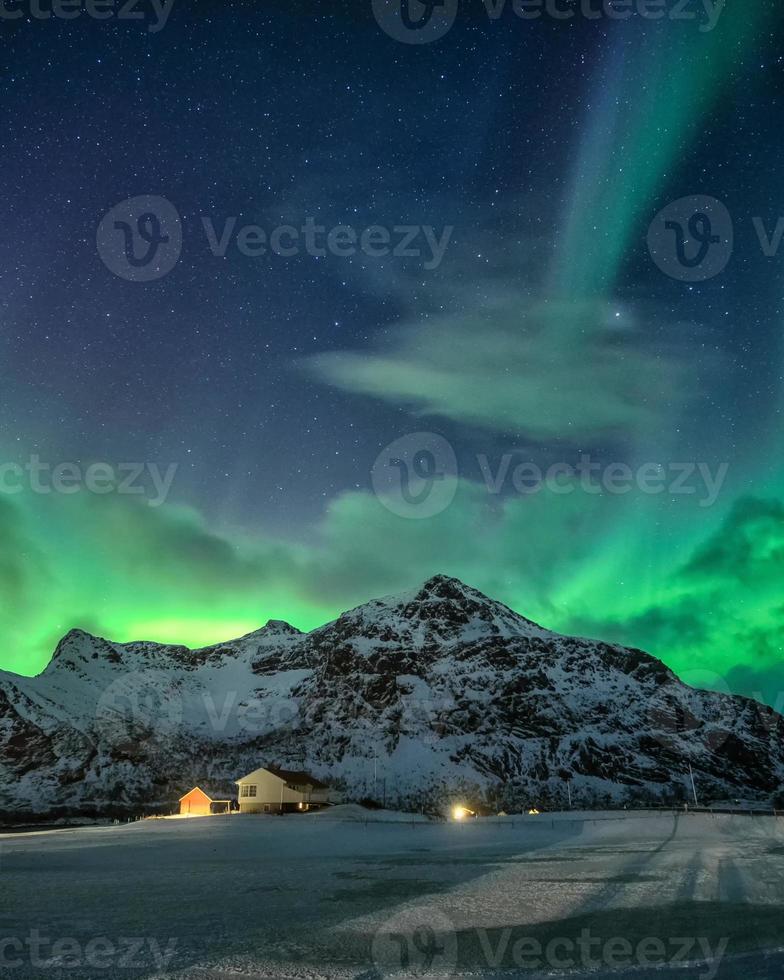 aurora boreal com estrelado sobre a montanha nevada e vila nórdica à noite em flakstad, ilhas lofoten foto