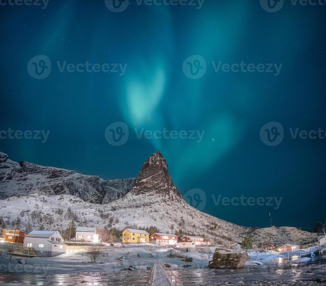 aurora boreal na montanha de neve com vila de pescadores nas ilhas lofoten foto