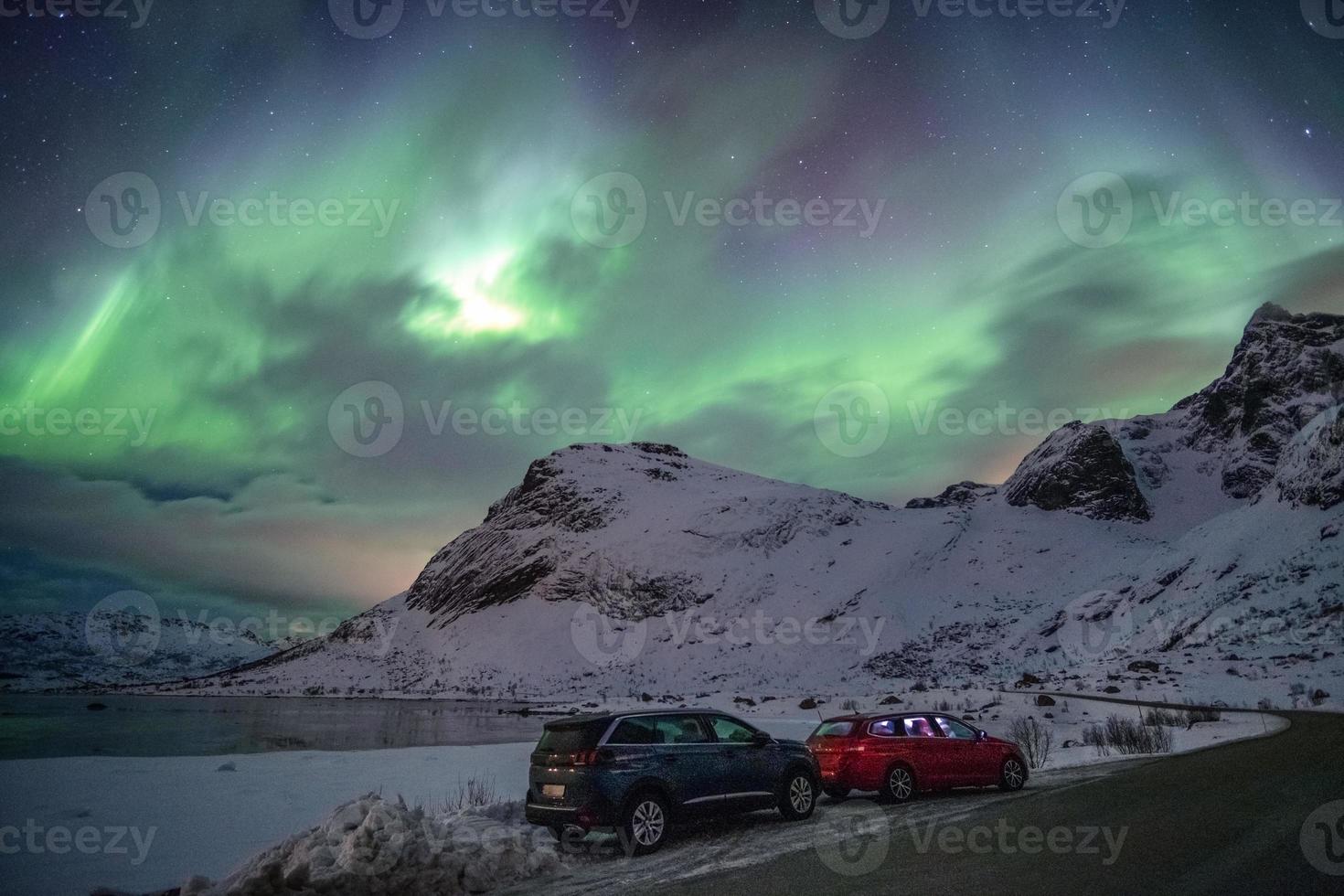 carros estacionados em estrada rural com aurora boreal no céu em lofoten foto