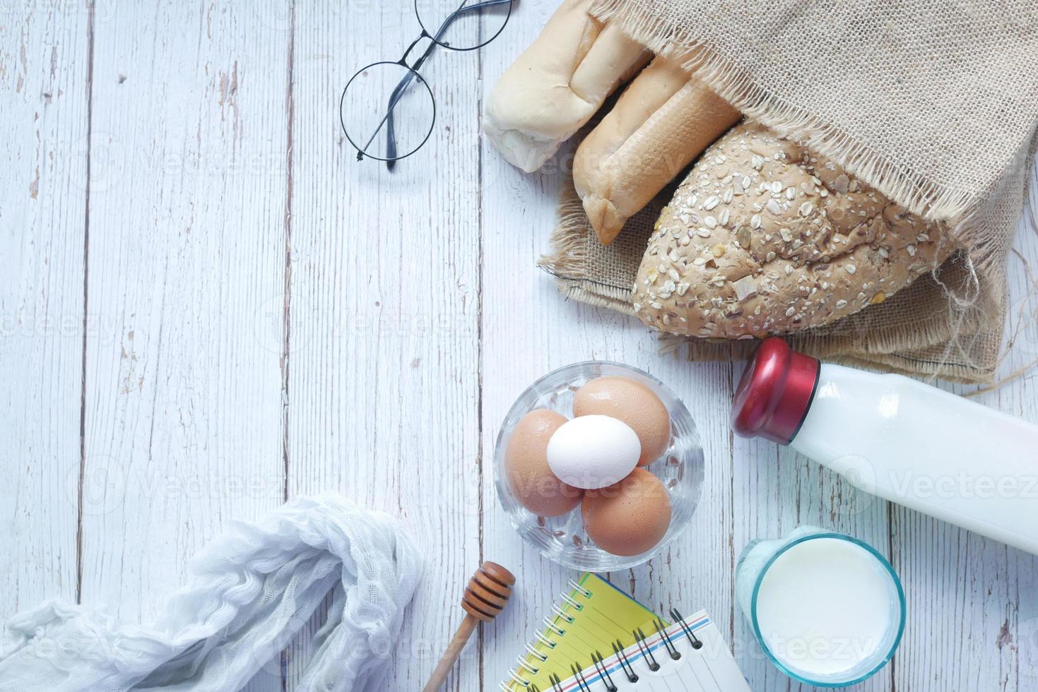 ovos em uma tigela, pão integral e leite na mesa foto