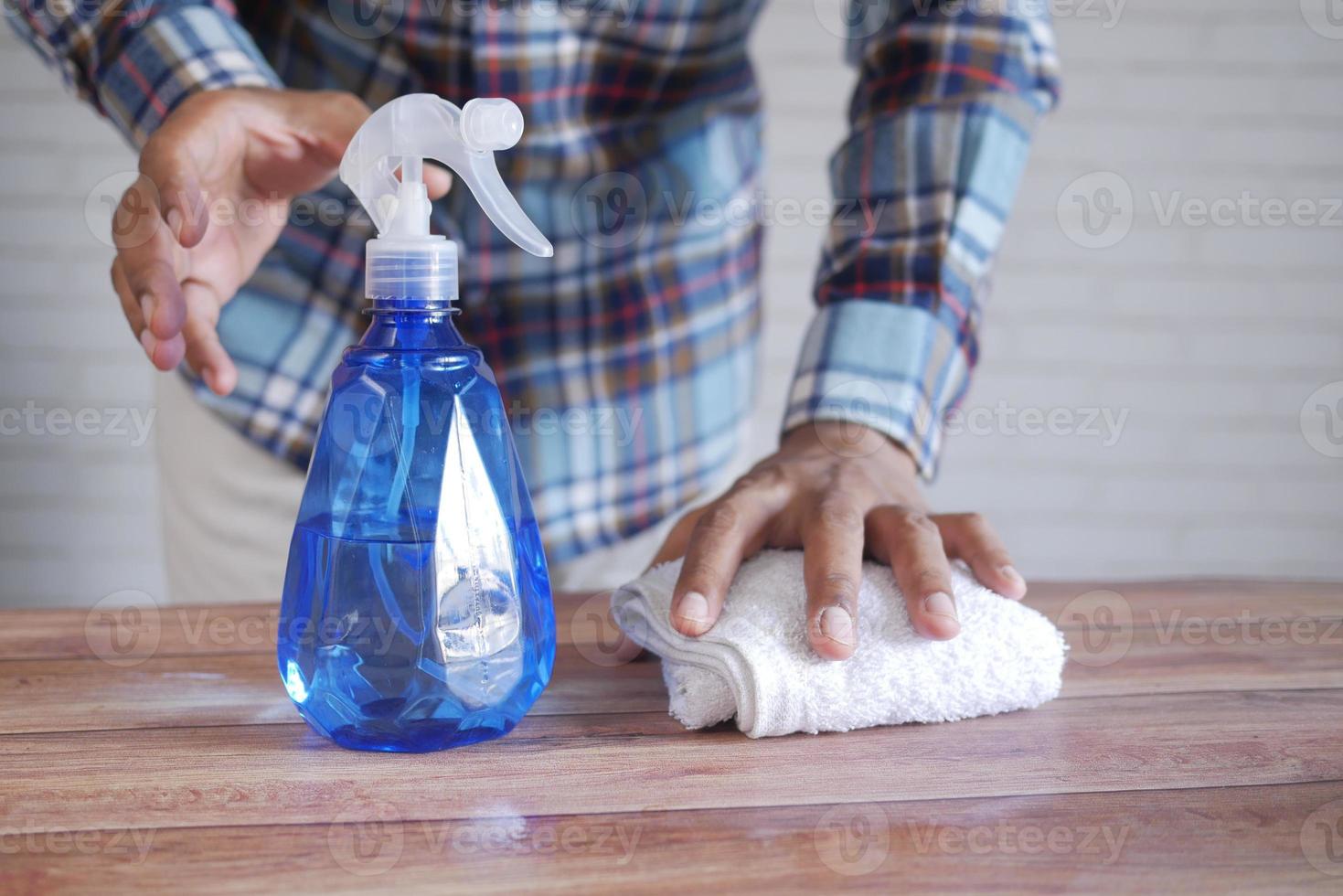 mão com luvas de borracha azul segurando frasco spray para limpar a mesa foto